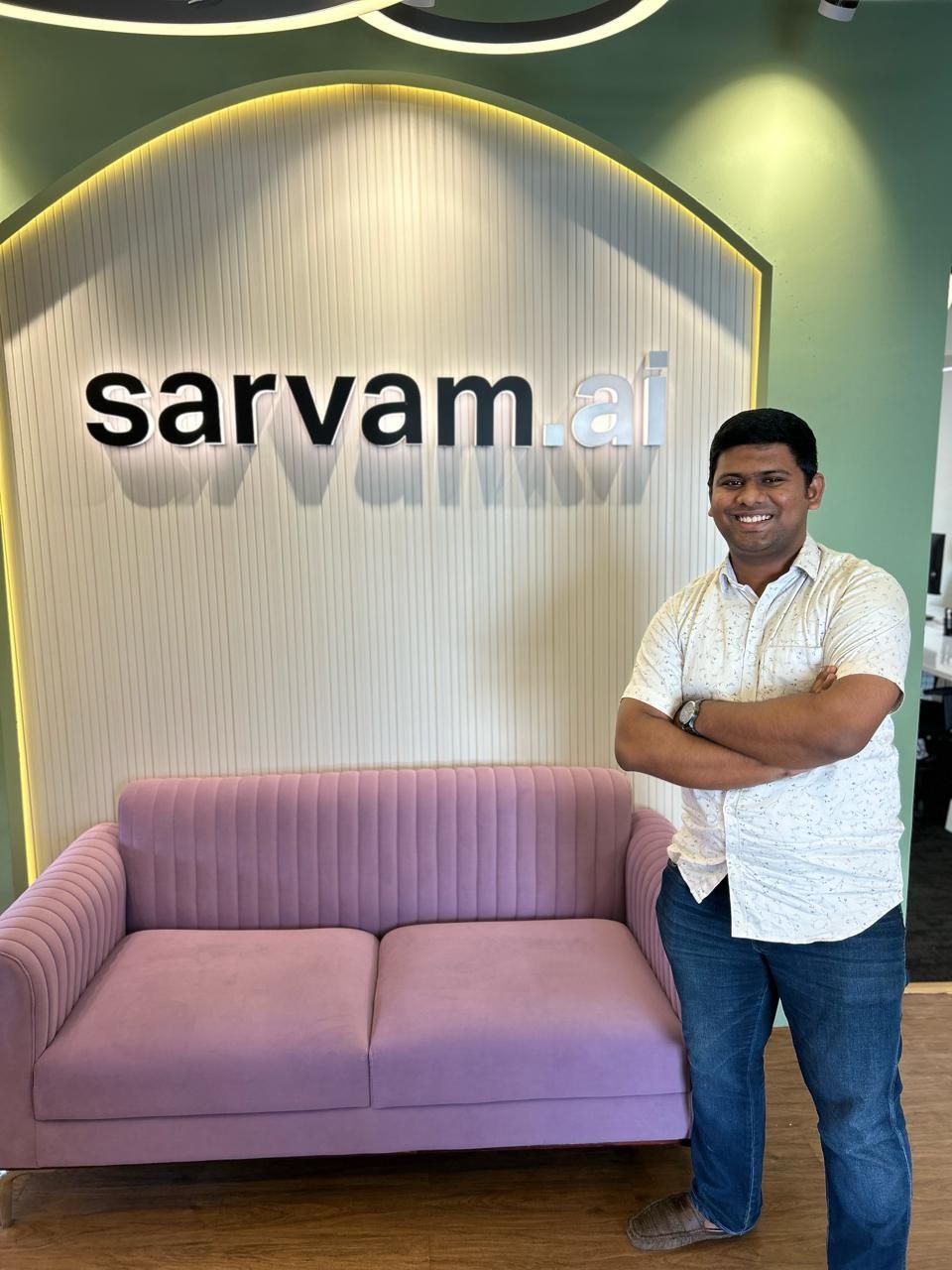 Kurian Benoy smiling and posing in front of Sarvam.ai logo in bangalore office